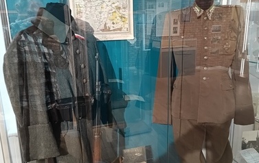 Szklana gablota z dwoma mundurami: niemieckim z pierwszej wojny światowej ozdobionym polskimi symbolami oraz polski  kawaleryjski z 1939 roku