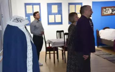 Uczestnicy wernisażu słuchający oprawadzającego po wystawie przewodnika; na pierwszym planie haftowany biały czepek