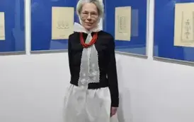 Kobieta w stroju ludowym pozująca na tle rysunk&oacute;w ze wzorami haft&oacute;