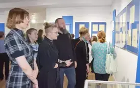 Dwie młode dziewczyny i chłopak stojący przy gablocie i oglądający eksponowane prace